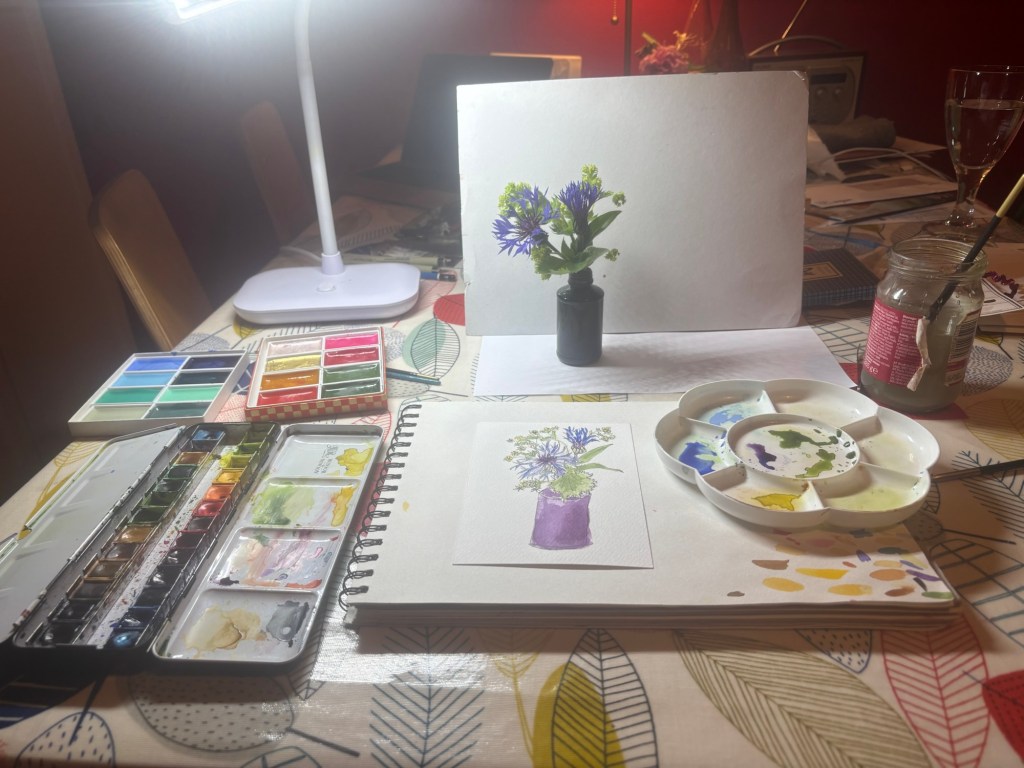 Scene of painting palette, small vase of flowers, a lamp and some other artists materials 